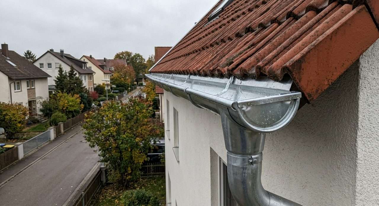 Reinigung einer Zink-Dachrinne an einem Wohnhaus